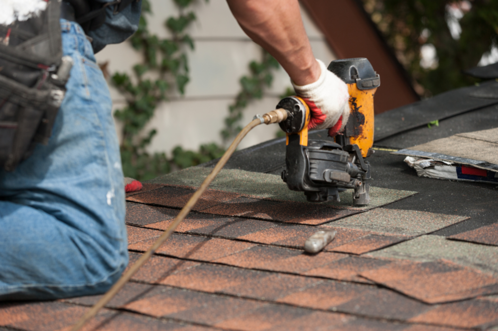 A man using a nailer for roof repair, illustrating the roof repair vs replacement decision process.